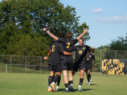 4 members of the UMBC soccer team cheer in a circling on the UMBC soccer field