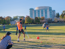 Students from student organization playing kickball outdoor on a field in front of the library.