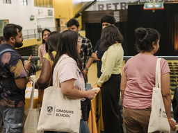 Group of students holding waiting in line at a graduate school event with tote bags that say UMBC graduate school.