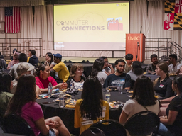 Diverse group of college students sitting at round tables talking during a commuter student welcome event.