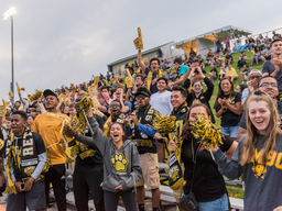 UMBC students dressed in UMBC gear cheering outside at a soccer game.