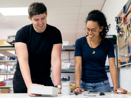 Two students standing and working with a piece of electronics equipment.