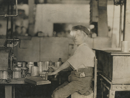 A person sits at a machine operating a tool to process metal cans in a factory setting.