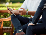 two persons seating in a bench outdoors, looking at a notebook